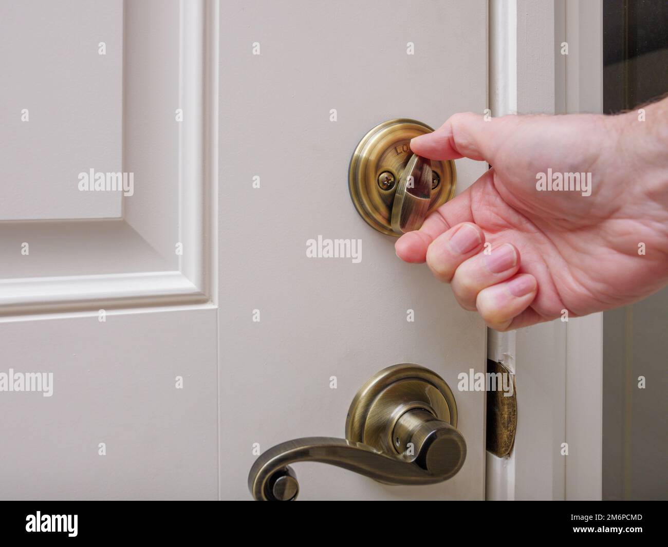 Nahaufnahme von Mann, der Türschloss mit Riegelverschluss an der weißen Eingangstür verriegelt. Haussicherheit Einbruch- und Diebstahlschutz. Stockfoto