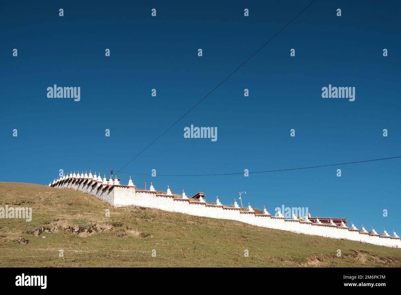 Tibetische Architektur. Traditionelle buddhistische Stupa im Sonnenlicht und blauem Himmel. Die Reihe der weißen tibetischen Stupa in der grünen Hügellandschaft. Stockfoto