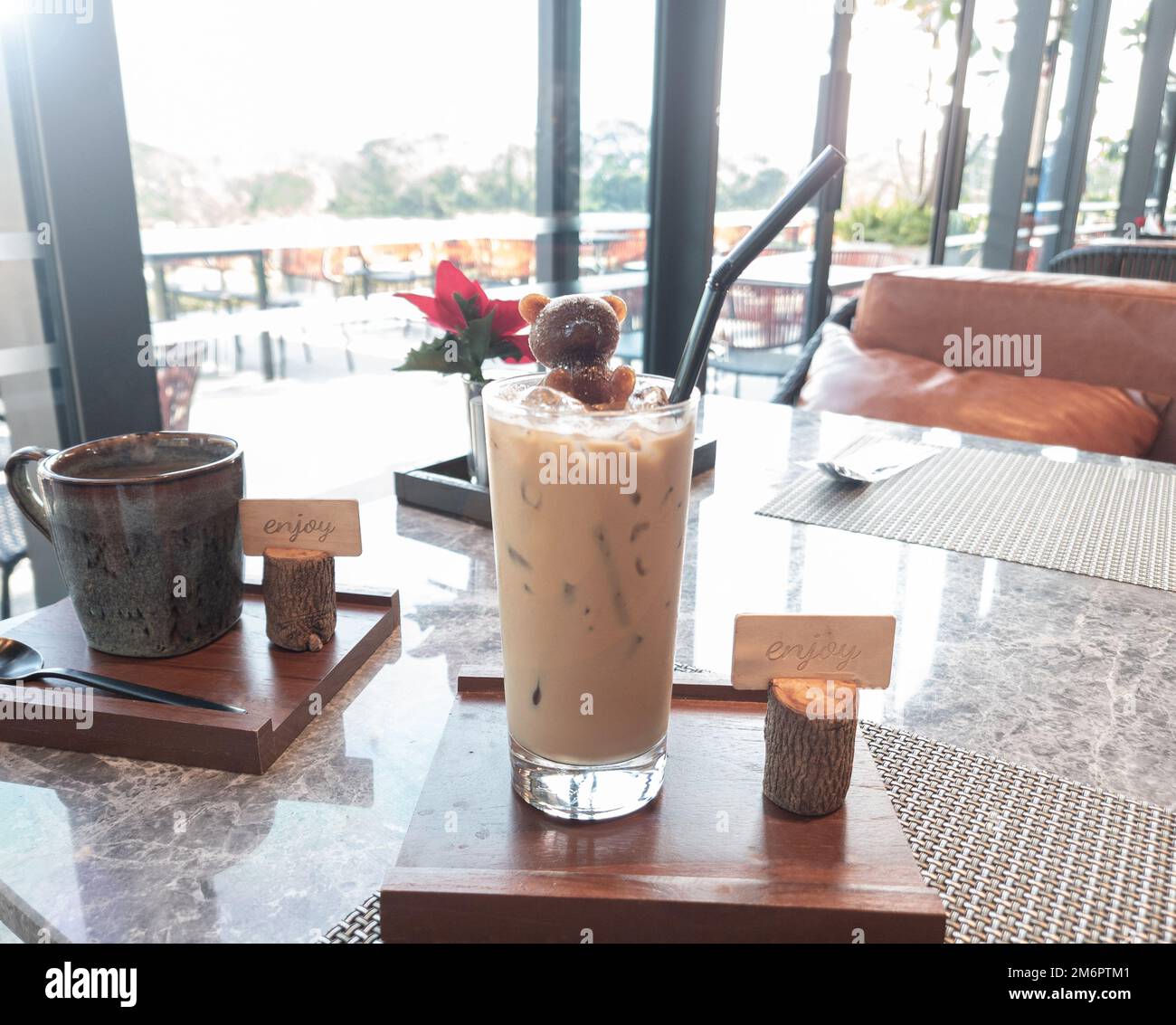 Ein Glas Latte-Kaffee mit einem Bärensirup-Eis auf Holzteller im Café und Blick auf den Außenbereich. Stockfoto