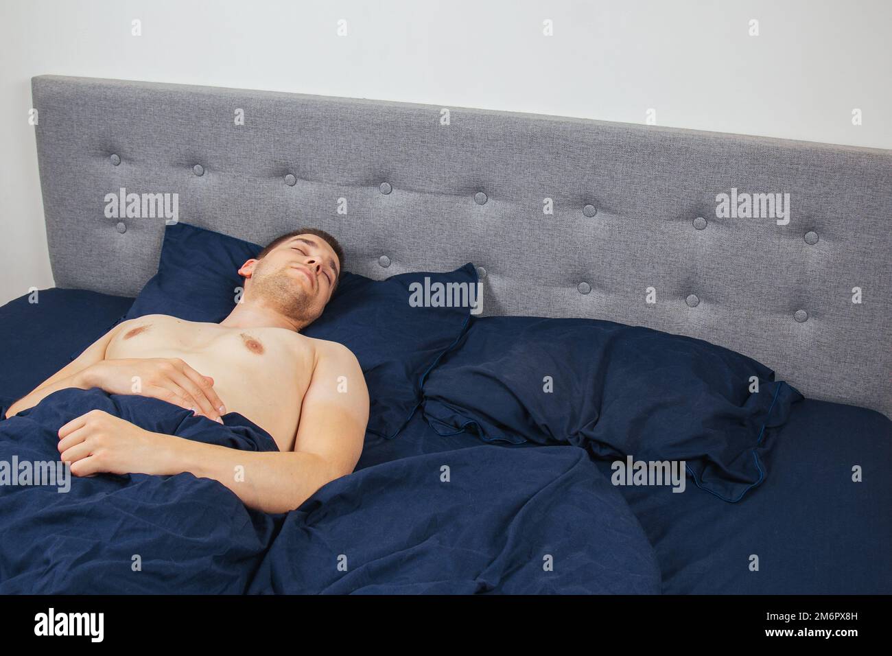 Ein gutaussehender junger Mann, der nachts ohne Kleidung auf dem Bett schläft. Junggesellenschlafzimmer. Tiefer Schlaf. Stockfoto