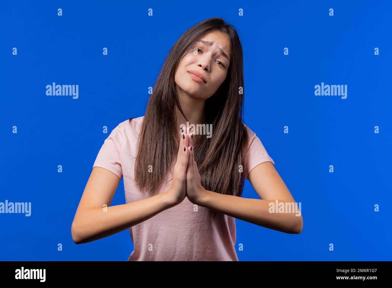 Junge Frau betet, bittet um Entschuldigung, sie ist schuldig. Blauer  Hintergrund. Ein hoffnungsvolles Gebetsmädchen, das jemanden bittet, seine  Wünsche zu befriedigen, ihm zu helfen Stockfotografie