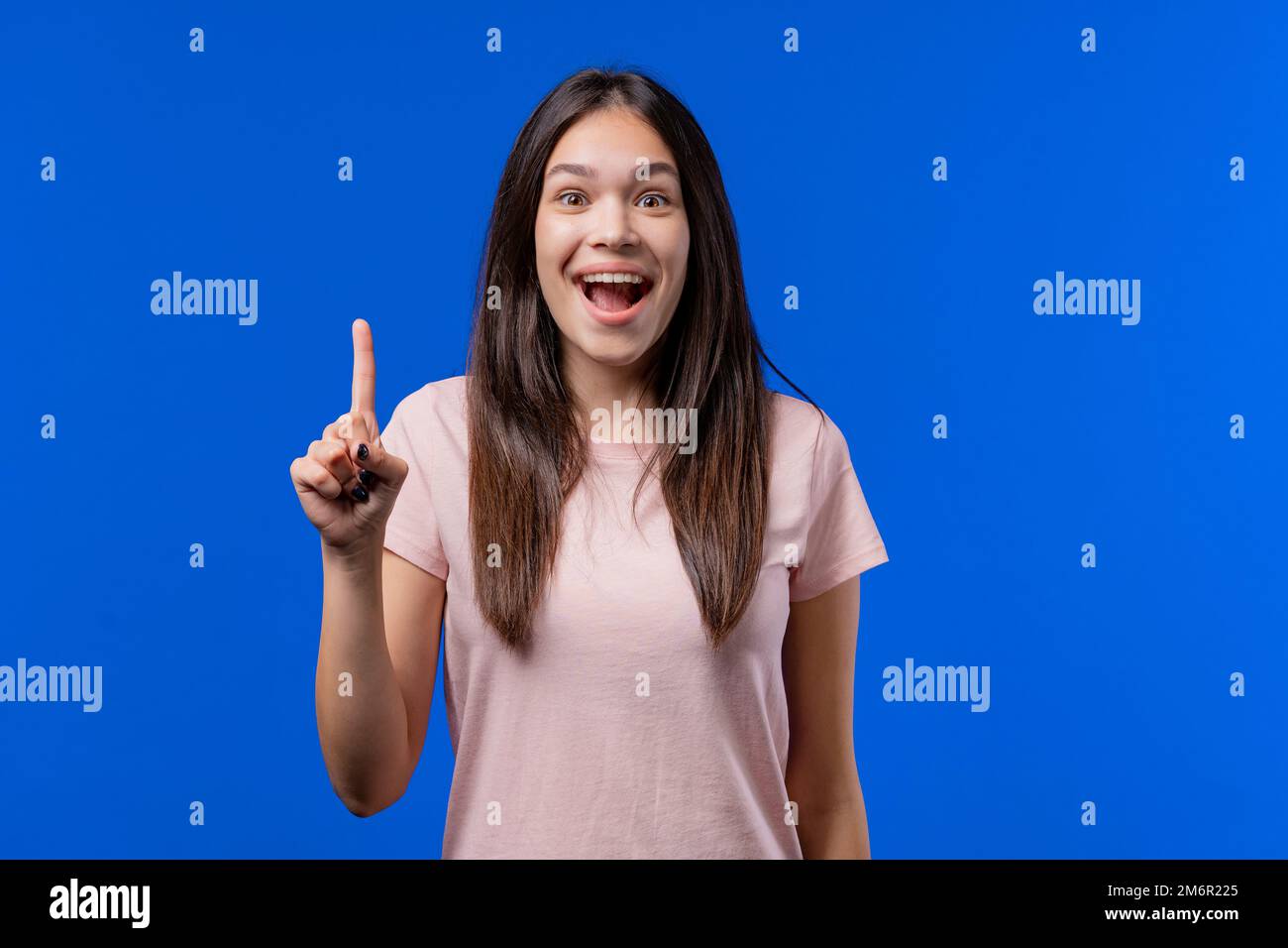 Glückliches Teenager-Mädchen, das sich den eureka-Moment vorstellt, mit dem Finger auf blauen Hintergrund zeigt. Eine kluge Studentin, die eine Antwort zeigt oder sich erinnert, was sie getan hat Stockfoto