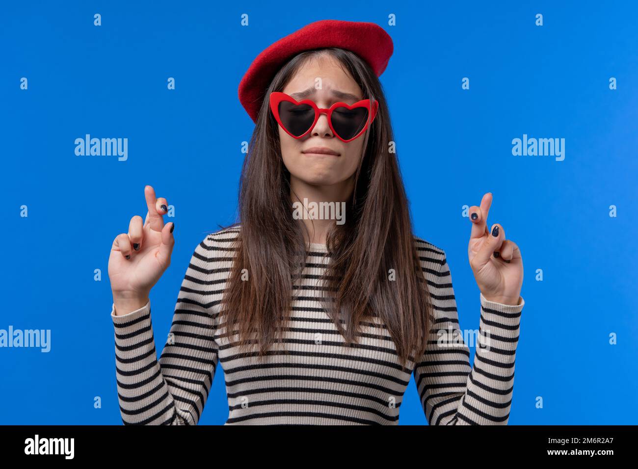 Hübsche Frau betet mit gedrückten Fingern auf blauem Hintergrund. Die Dame bittet jemanden, der ihre Wünsche befriedigt, hilft, betet für ihr Glück in der Prüfung Stockfoto