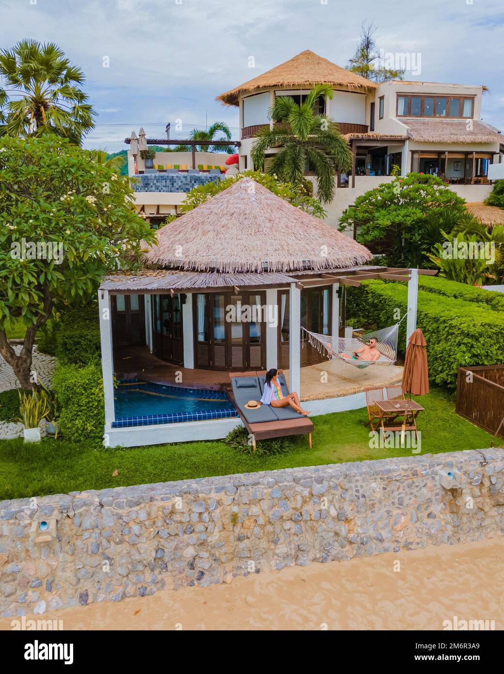 Ein Paar in einer luxuriösen Villa, die sich am Pool mit Blick auf das Meer und den Strand erholt Stockfoto