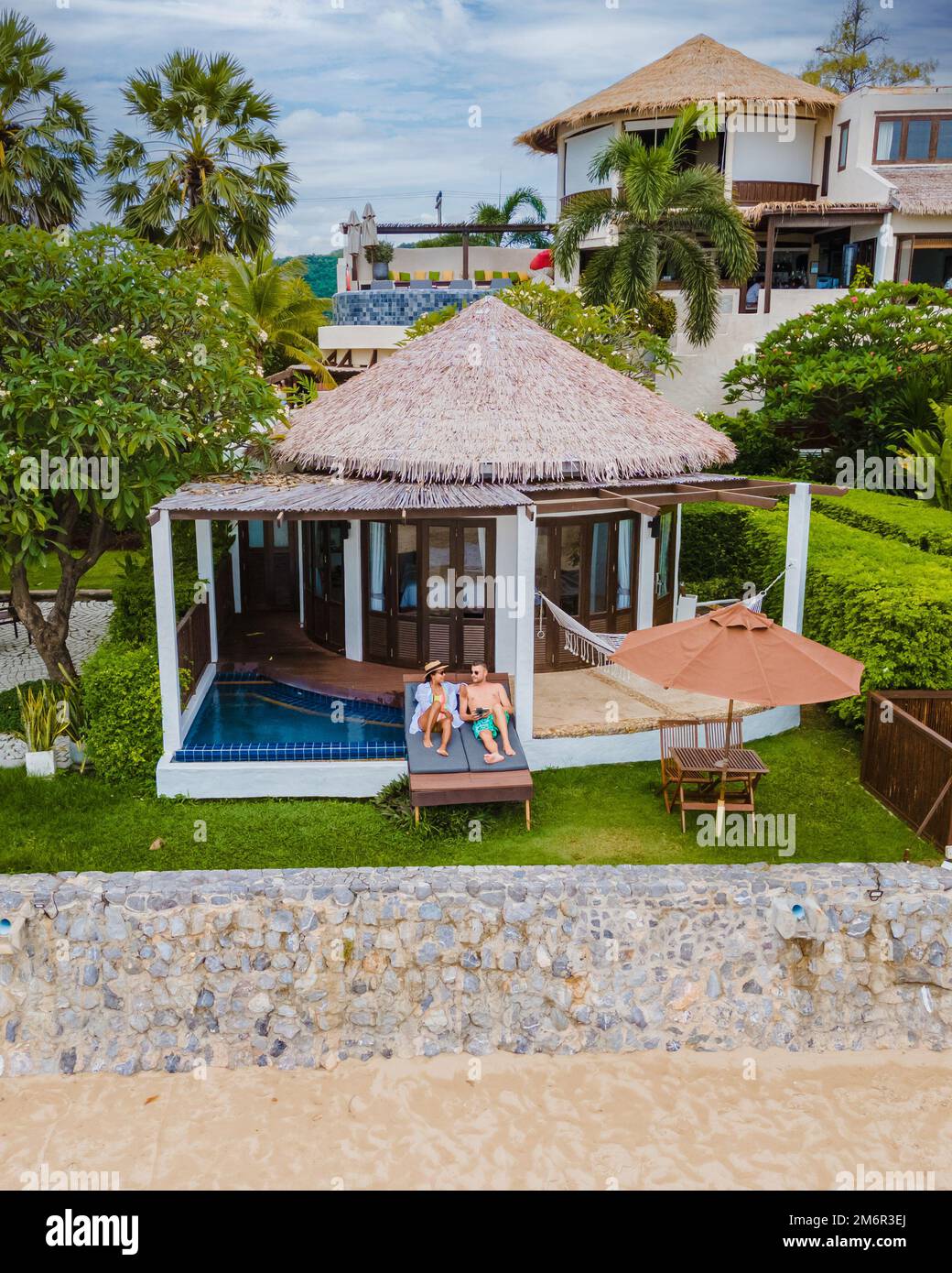 Ein Paar in einer luxuriösen Villa, die sich am Pool mit Blick auf das Meer und den Strand erholt Stockfoto