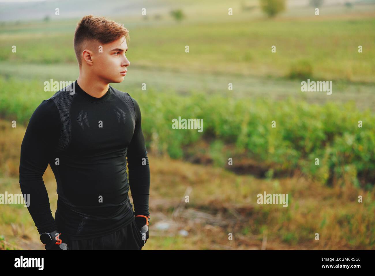 Der gutaussehende Sportler in einem Sportanzug bewundert die Schönheit eines Feldes, bevor er mit seinem morgendlichen Training beginnt Stockfoto