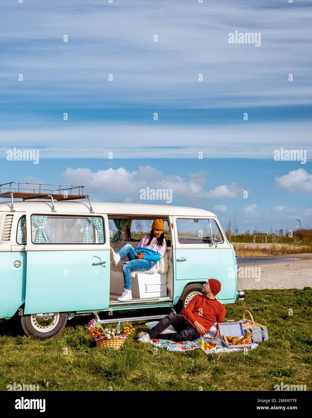 Der alte Vintage Camper Van parkte am See mit ein paar Männern und Frauen, die den Sonnenaufgang beobachteten Stockfoto