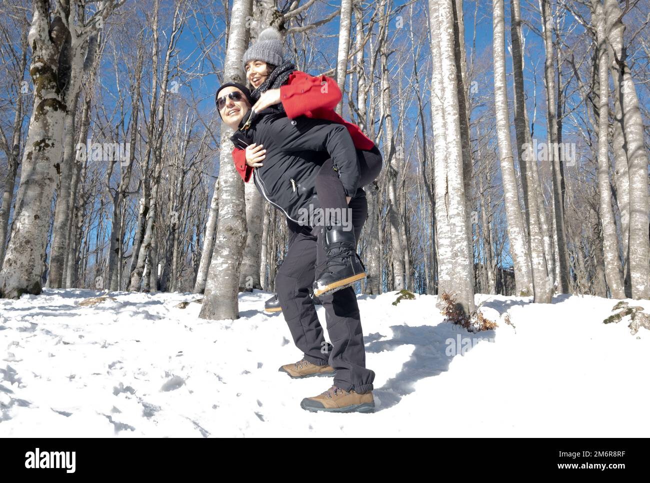 Glückliches junges Paar im Winterwald. Ein Mann, der Huckepack-Frauen-Ritt gibt. Mount Amiata, Toskana, Italien Stockfoto