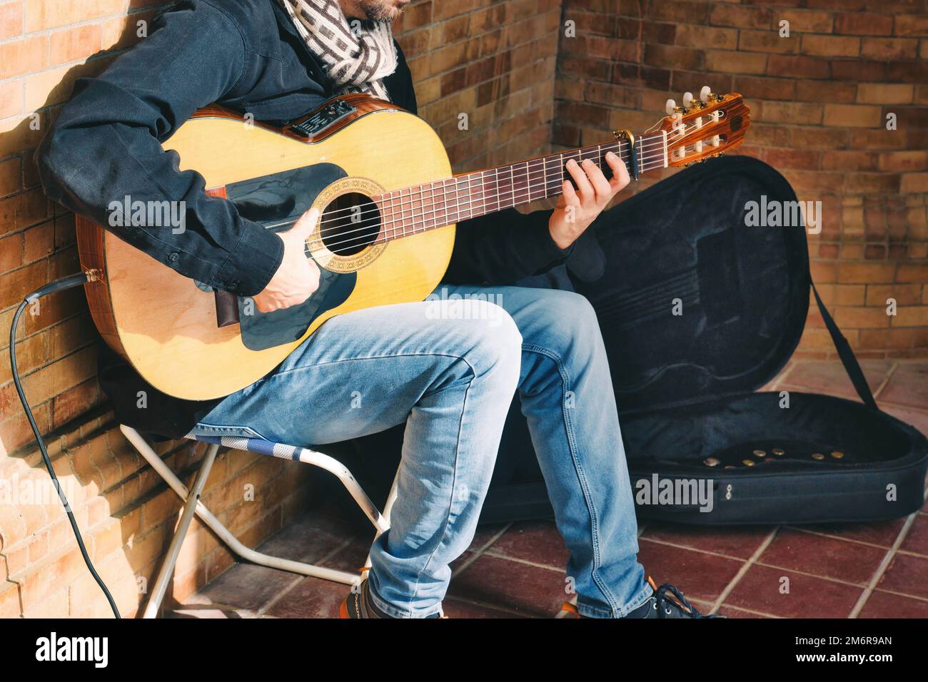 Ein männlicher Streuner, der spanische Akustikgitarre spielt, mit einem kleinen Verstärker auf der Straße Stockfoto