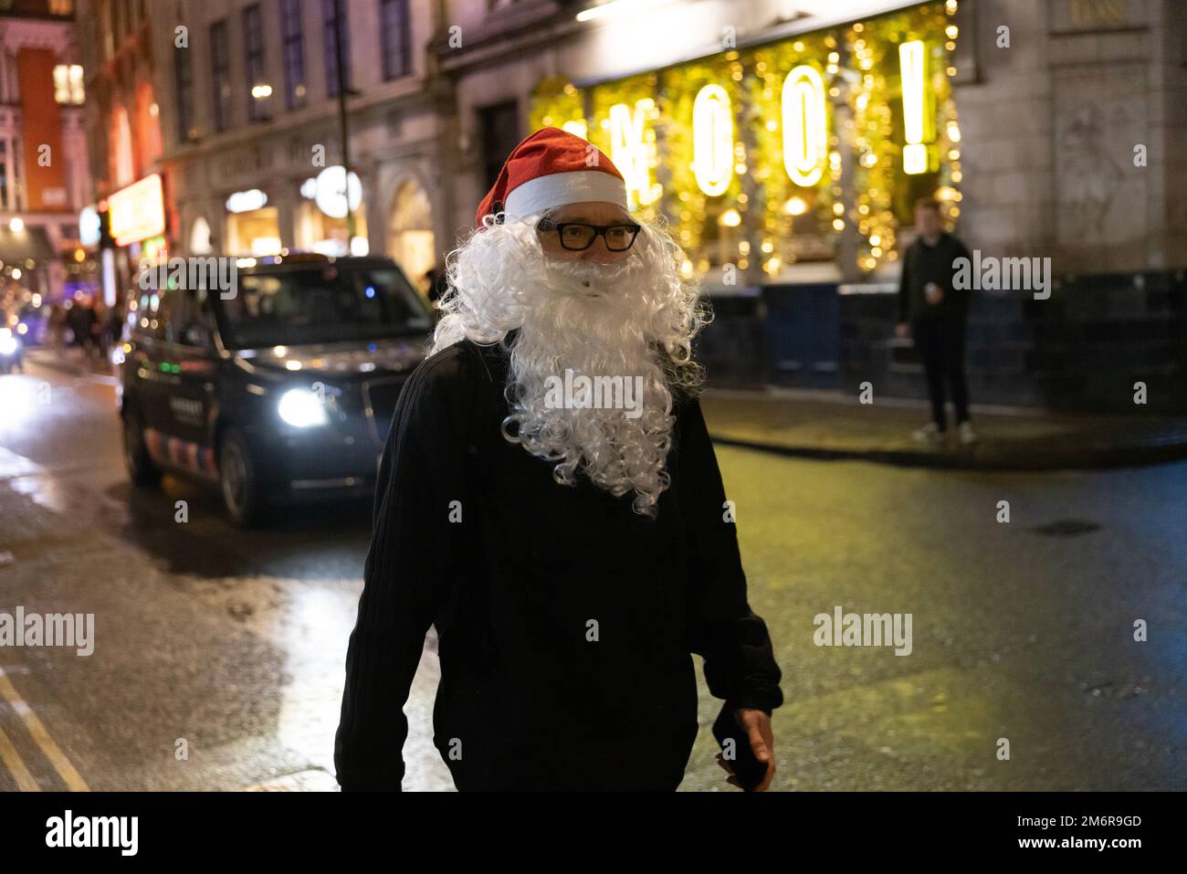 Mann mit Weihnachtsmannmütze und -Bart, Old Compton Street, Soho bei Nacht, auf dem Weg zu Weihnachten 2022, London, England, Großbritannien Stockfoto