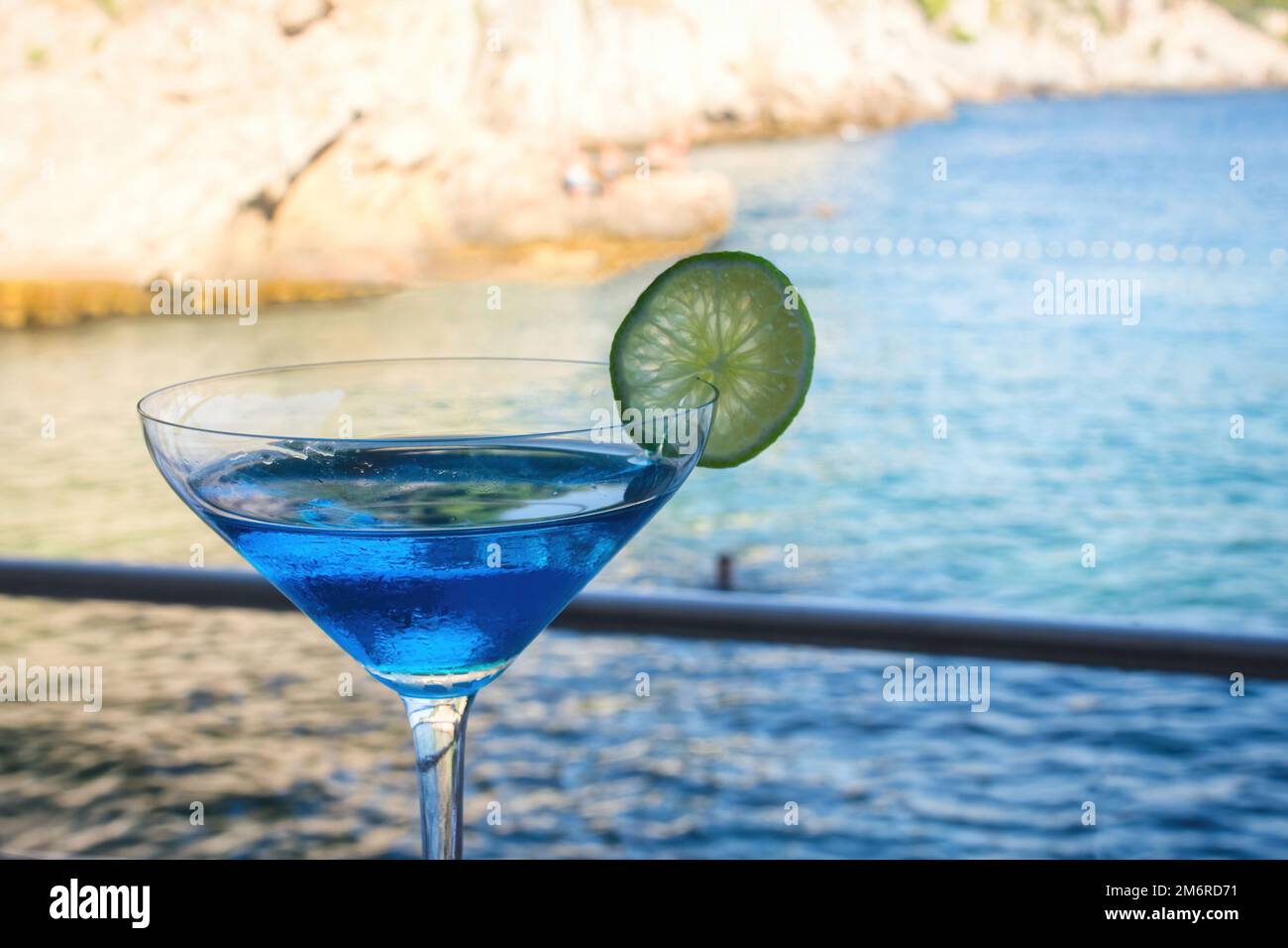 Ein blauer Cocktail in einem hohen Glas vor einem verschwommenen Hintergrund mit blauem Wasser am Strand Stockfoto