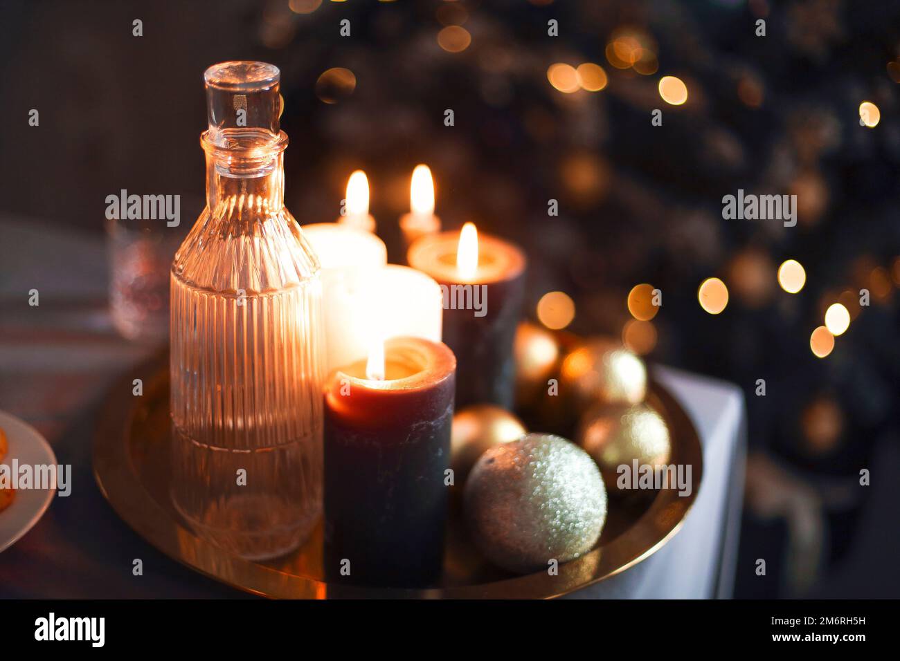 Silvester-Stillleben. Gläser und eine Karaffe aus transparentem Glas, Kerzen und goldener Weihnachtskugel Stockfoto