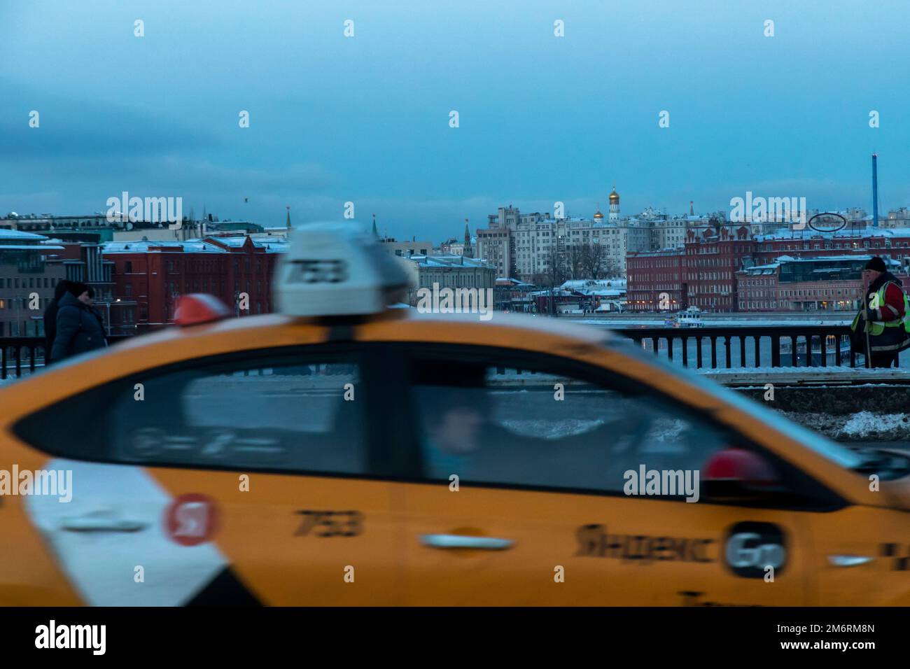 Moskau, Russland. 5. Januar 2023. Ein gelbes Taxi mit der Aufschrift „Yandex Taxi“ fährt auf der Krimbrücke vor dem Hintergrund eines Panoramablicks auf das Zentrum von Moskau, Russland Stockfoto