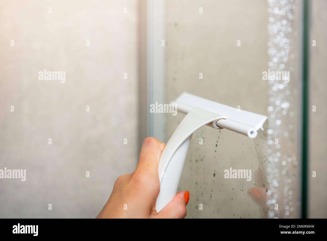 Reinigung der Duschkabine. Reinigung der Glaswand der Duschkabine mit einem Glasschaber. Das Haus putzen, das Bad und die Dusche pflegen. Stockfoto