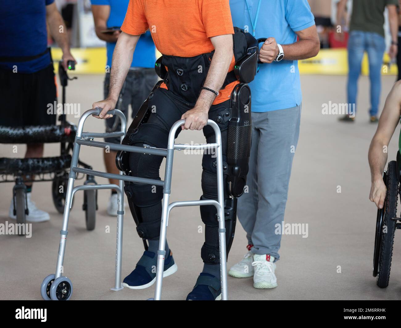 Junge mit Bewegungsproblemen in den unteren Gliedmaßen in aufrechte Haltung Gehen dank eines mechanischen Exoskeletts und mit Hilfe seines Physiotherapeuten. Stockfoto