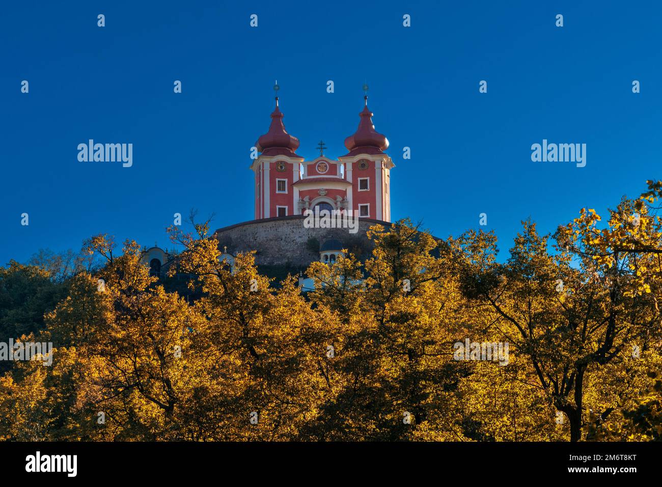 Blick auf die rote Calvary Banska Stiavnica unter blauem Himmel mit Herbstwald im Vordergrund Stockfoto