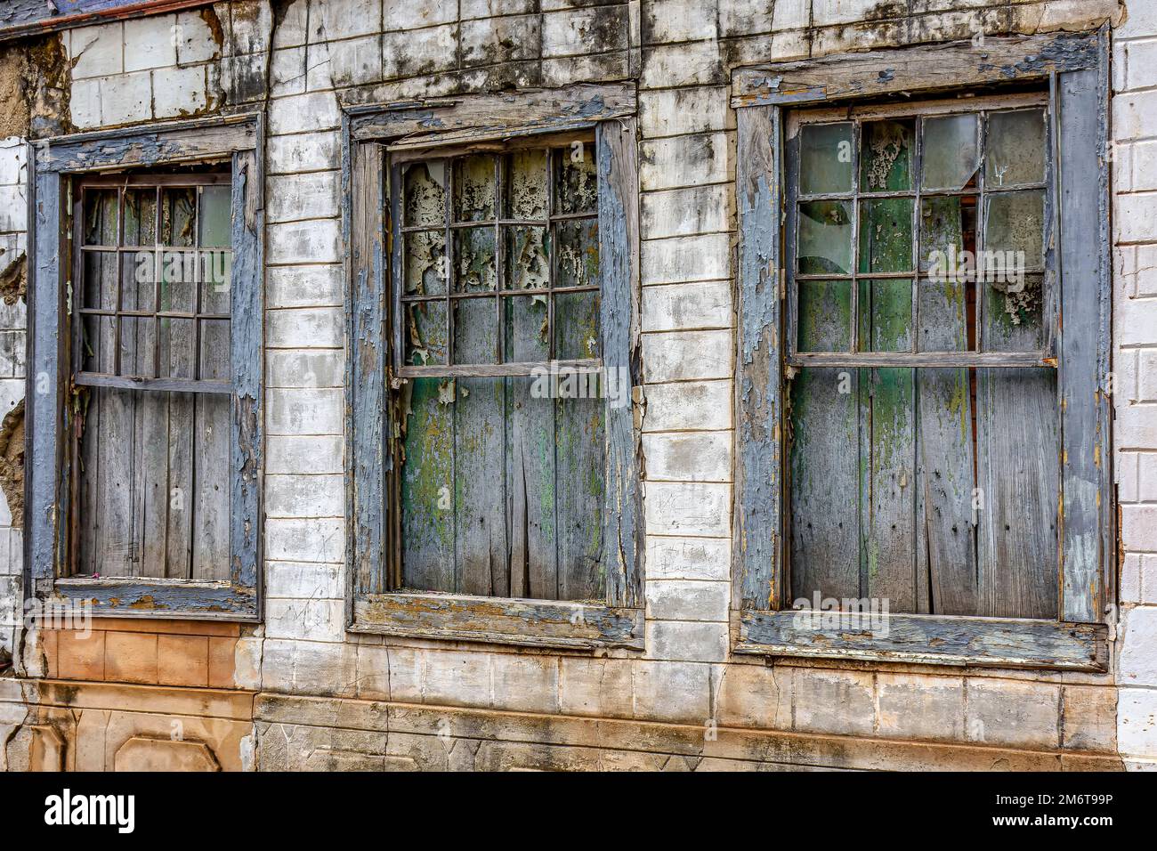 Alte Holzfenster, die durch die Zeit an der Fassade eines verlassenen Hauses ruiniert wurden Stockfoto