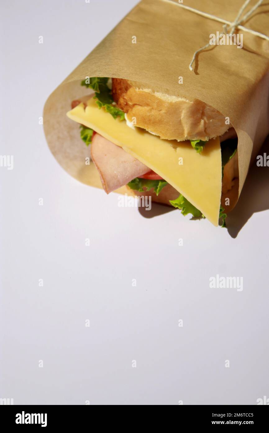 Sandwich mit Käse und Schinken, in Papier eingewickelt auf weißem Hintergrund mit Kopierbereich Stockfoto