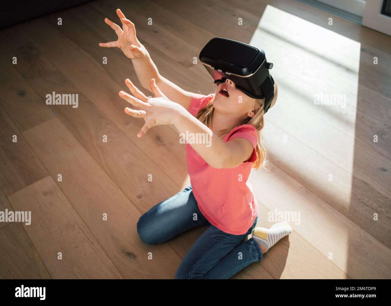 Kaukasische Frau in einem Virtual-Reality-Headset, die auf dem Boden des Wohnzimmers sitzt und sich auf die virtuelle Welt freut Stockfoto