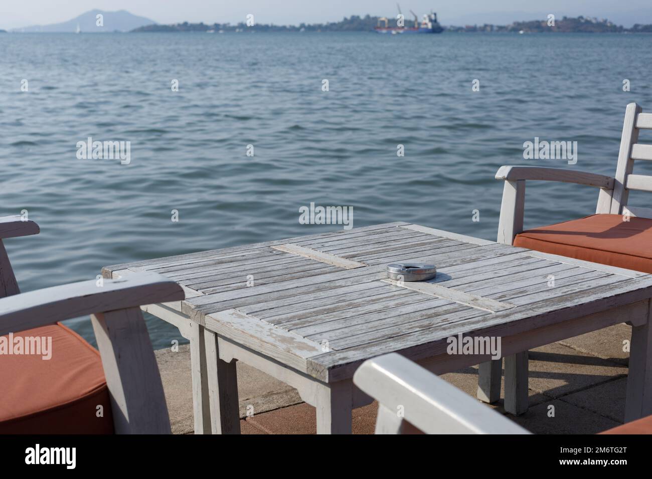 Ein Tisch in einem Freiluft-Restaurant mit Blick auf das Meer. Esstisch aus Holz und Holzstühle mit Kissen. Restaurant im Freien mit Meerblick Stockfoto