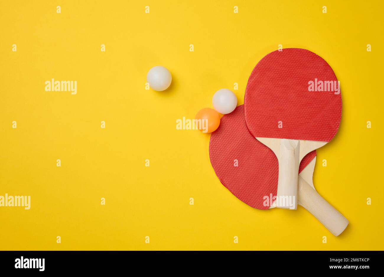 Ein Paar Tennisschläger aus Holz für Tischtennis und Plastikbälle auf gelbem Hintergrund Stockfoto