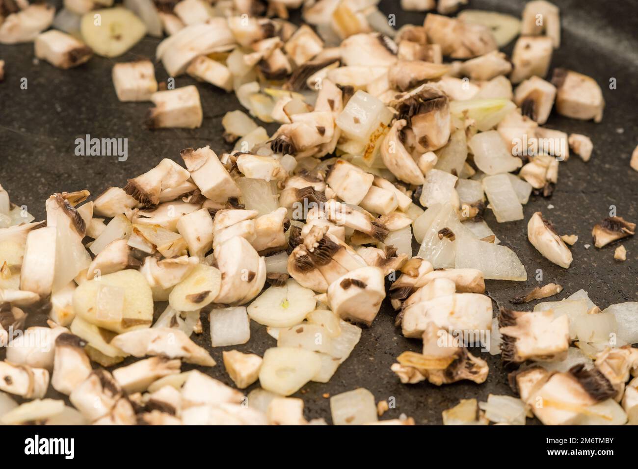 Sie kochen gehackte Zwiebeln und Pilze in einem Kochtopf Stockfoto