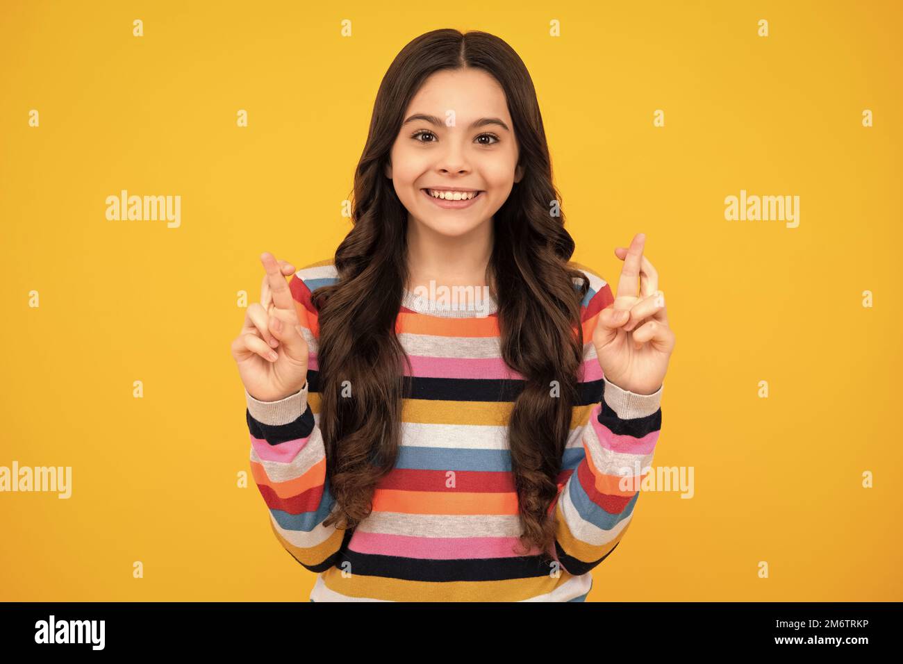 Teenager Kind Mädchen, die ihre Finger kreuzt und viel Glück wünscht, isoliert auf gelbem Studiohintergrund mit Kopierraum. Glücklicher Teenager, positiv und Stockfoto
