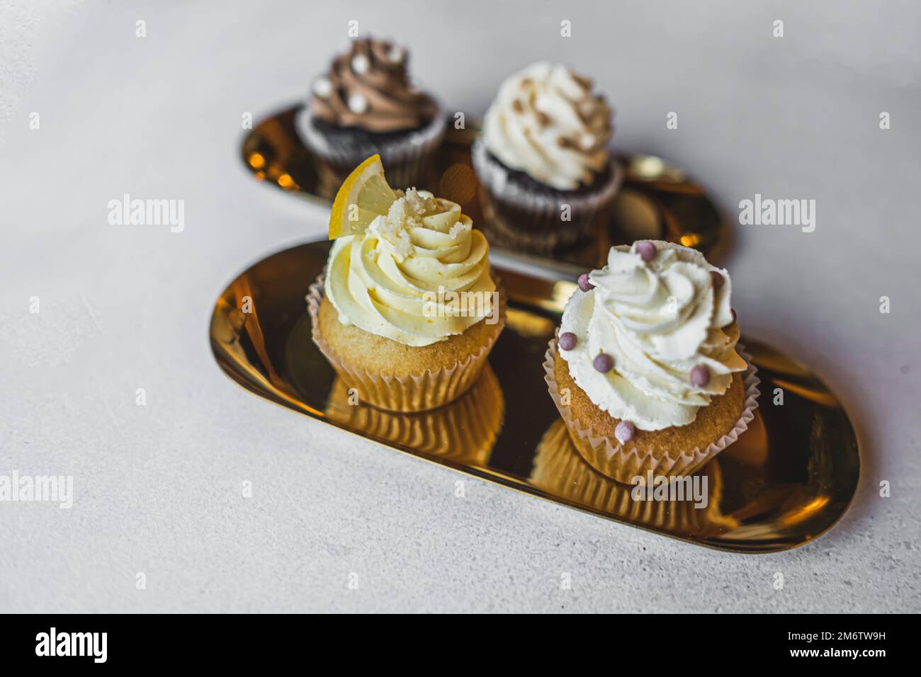 Nahaufnahme künstlerischer Cupcakes mit Buttercreme-Zuckerguss und Dekorationen auf goldenen Tellern. Speicherplatz kopieren. Hochwertiges Foto Stockfoto