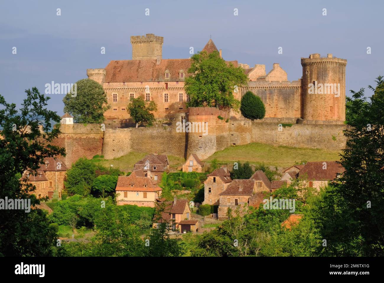 Castelnau: Leuchtend rote und orangefarbene Steine der Stadt und Burg Castelnau-Bretenoux kurz nach Sonnenaufgang in Castelnau-Bretenoux, Lot, Frankreich Stockfoto