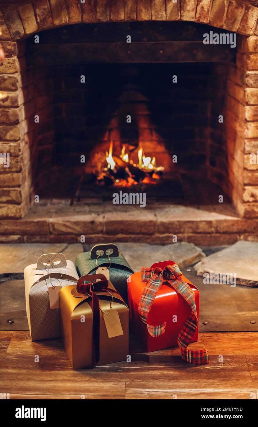 Vier verpackte Weihnachtsgeschenke auf Holzboden in der Nähe eines brennenden Kamins Stockfoto