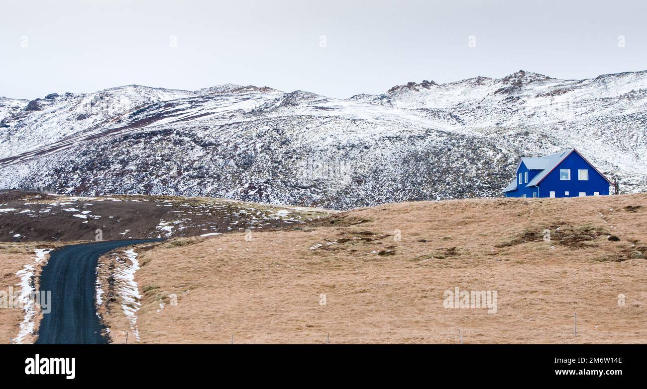 Islandschaft mit blauem Chalet-Bauernhaus auf der Halbinsel Reykjanes. Berge bedeckt mit Schnee i Stockfoto