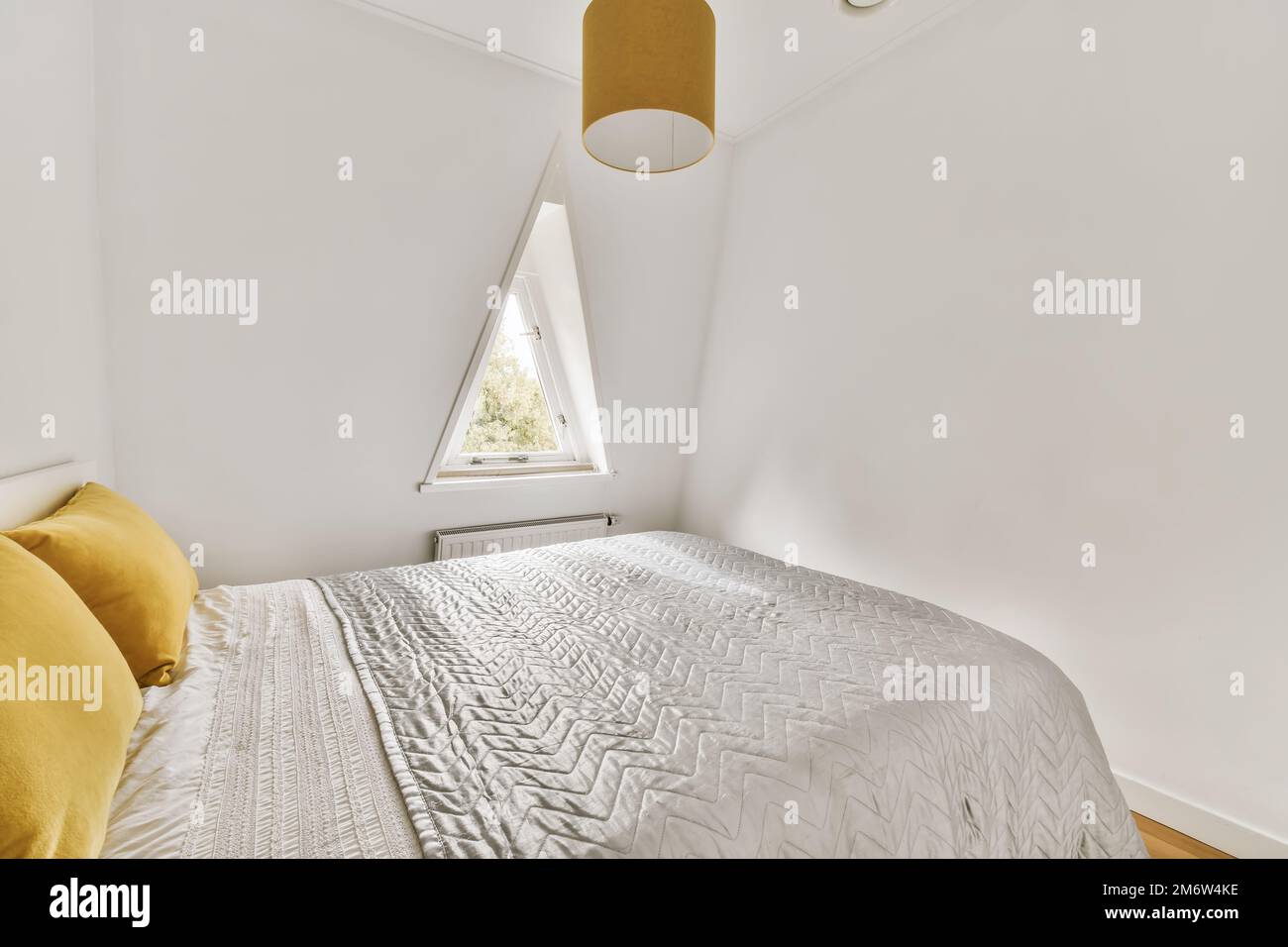 Ein Schlafzimmer mit weißen Wänden und Holzfußboden das Zimmer hat ein großes Bett und gelbe Überwurf-Kissen darauf Stockfoto