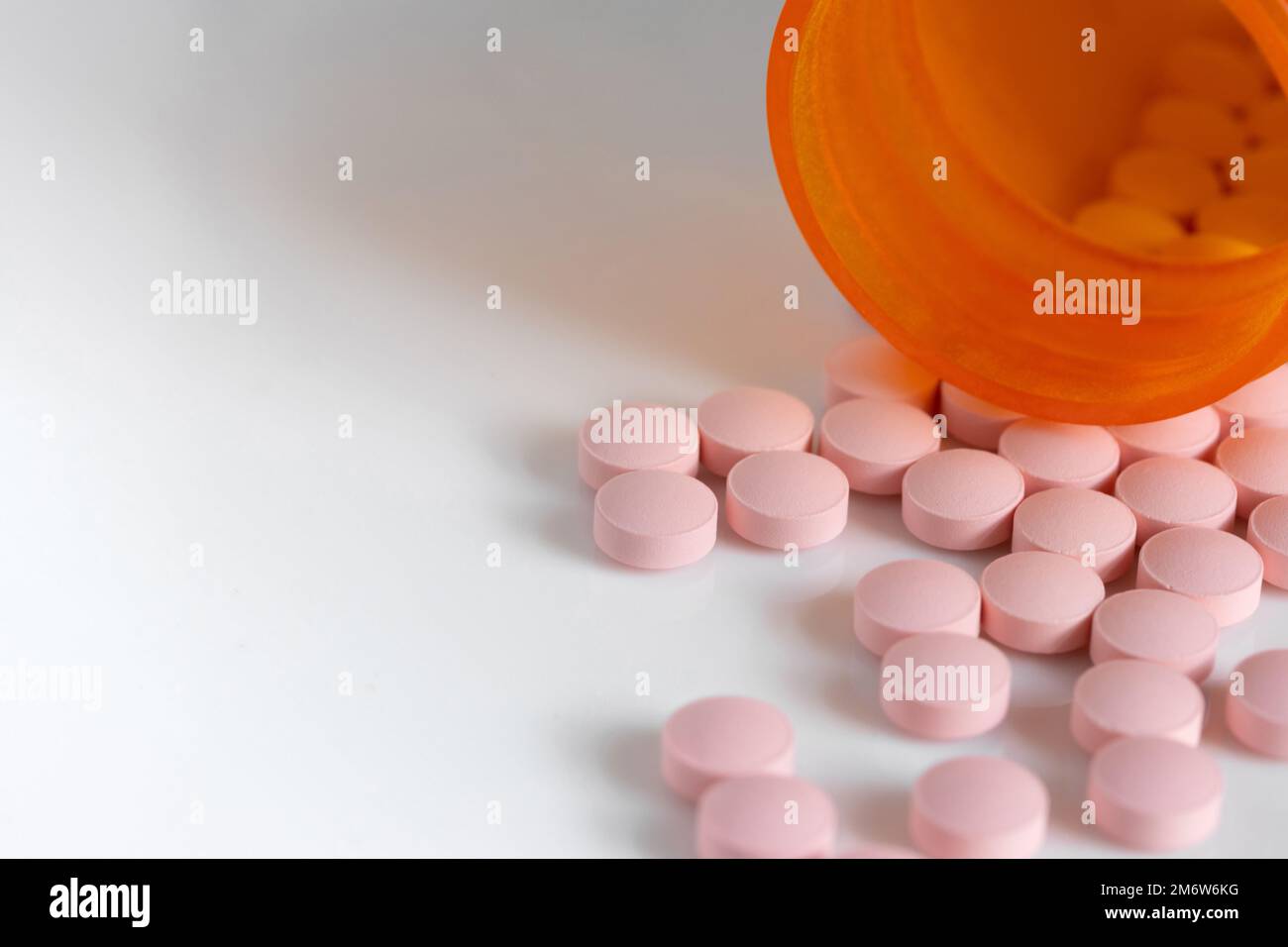 Rosafarbene Tablettentabletten aus einer Arzneimittelflasche auf weißem Hintergrund mit Kopierraum und geringer Schärfentiefe Stockfoto