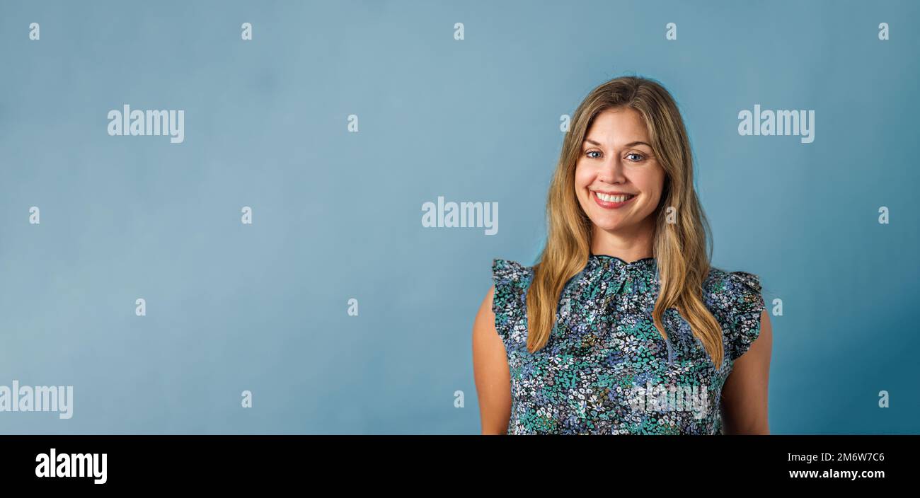 Eine attraktive brünette Frau in ihren Vierzigern, die ein geblümtes Oberteil mit blauem Bannerhintergrund und Kopierbereich trägt Stockfoto