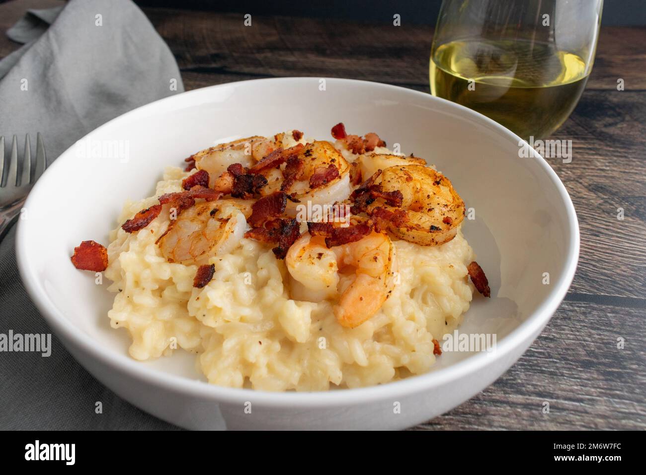 Cremige Garnelen Risotto mit Speck und einem Glas Weißwein aus nächster Nähe: Ein dekadentes Gericht mit Schalentieren, Reis und cremigem Käse Stockfoto