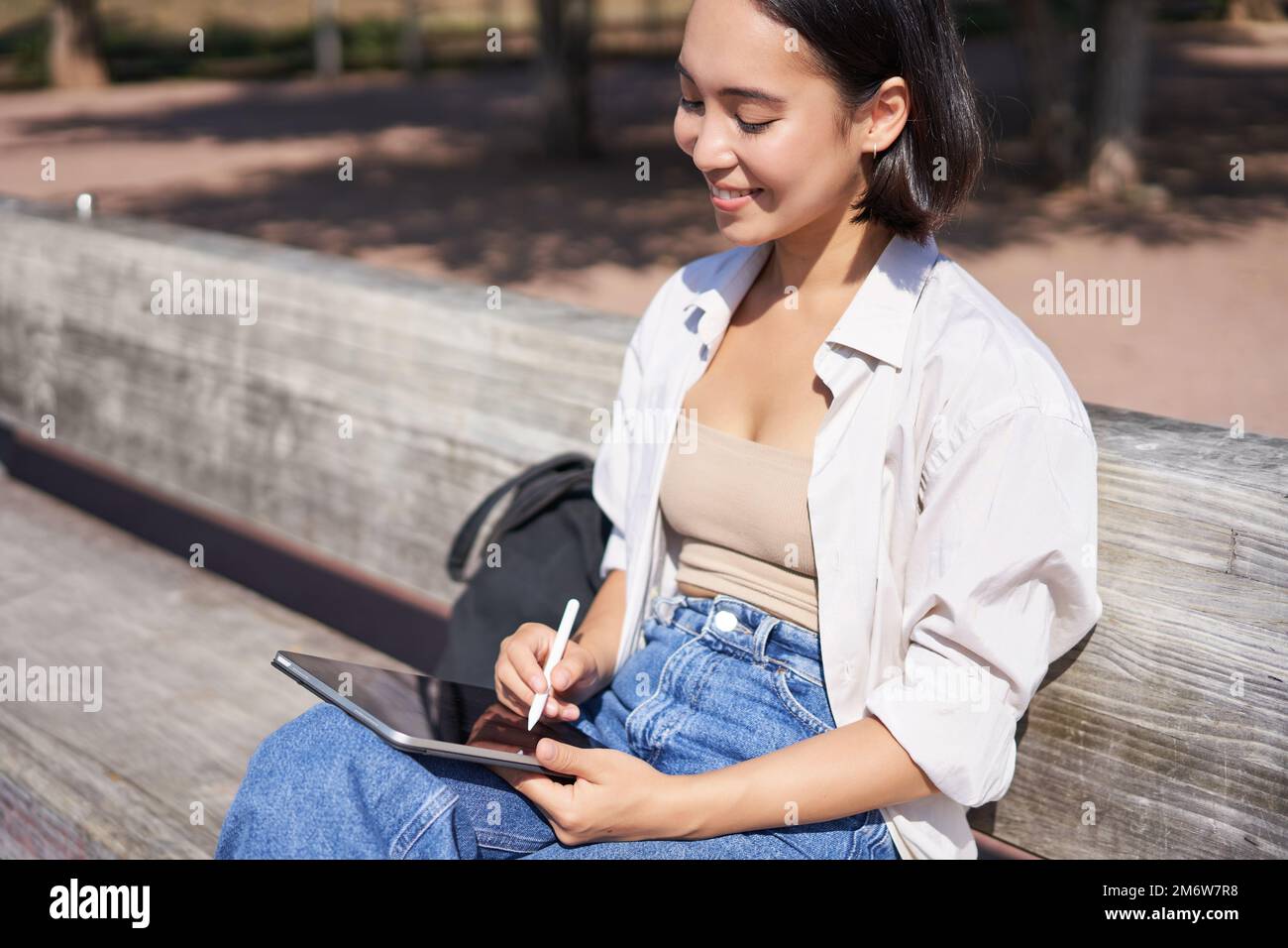 Junge asiatische kreative Mädchen Zeichnung mit Stift auf Grafik-Tablet, sitzen im Freien im Park, Malerei smth Stockfoto