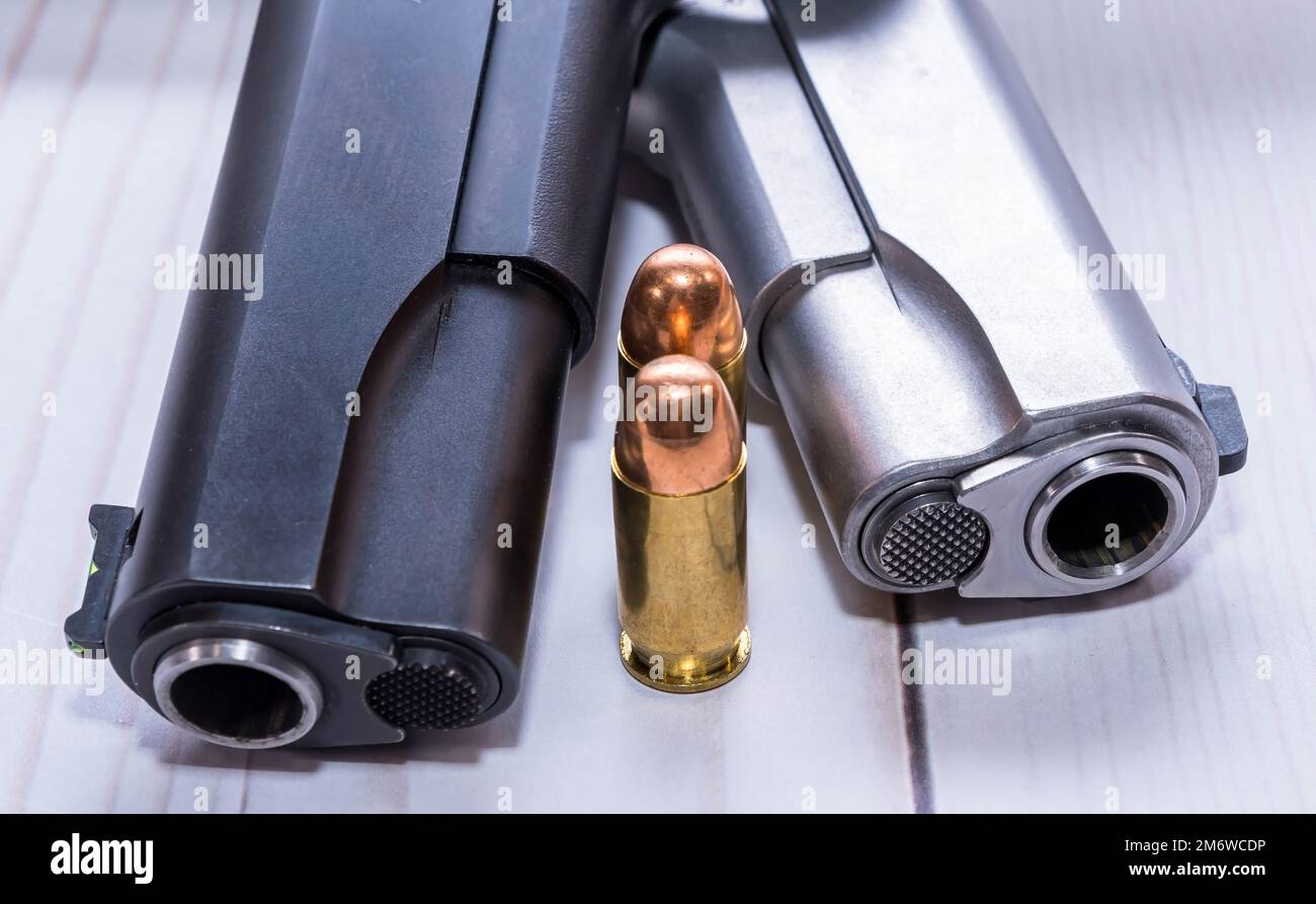 Die Maulkörbe von zwei verschiedenen 1911-Pistolen, die in 45ACP kammerten, eine schwarze und die andere aus rostfreiem Stahl, zusammen mit zwei Kugeln für sie Stockfoto
