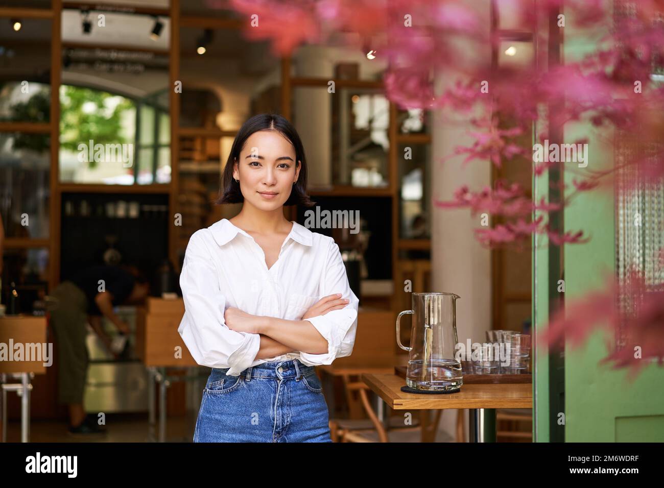 Porträt einer jungen Geschäftsfrau in ihrem eigenen Café, der Manager steht neben dem Eingang und lädt Sie ein, posiert in weißem Hemd und Stockfoto