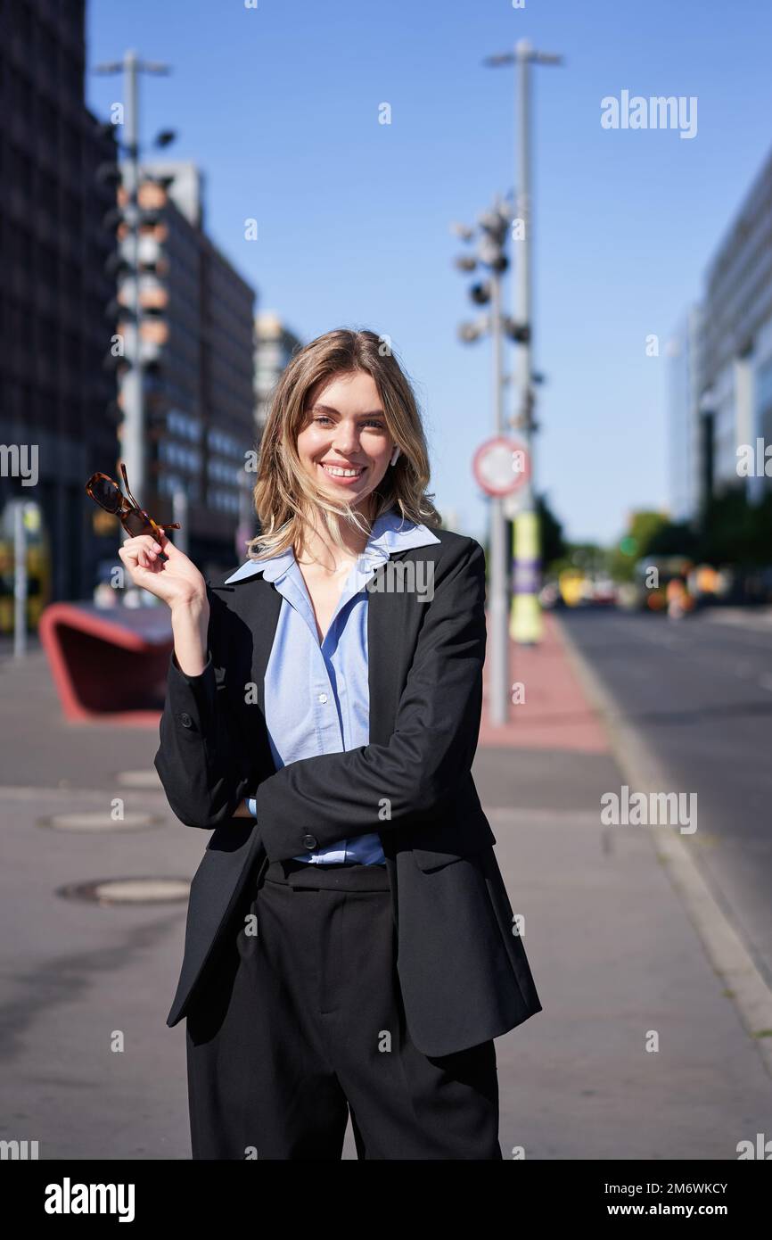 Porträt einer erfolgreichen jungen geschäftsführerin, Geschäftsfrau in schwarzem Anzug, auf einer sonnigen Straße stehend und lächelnd Stockfoto
