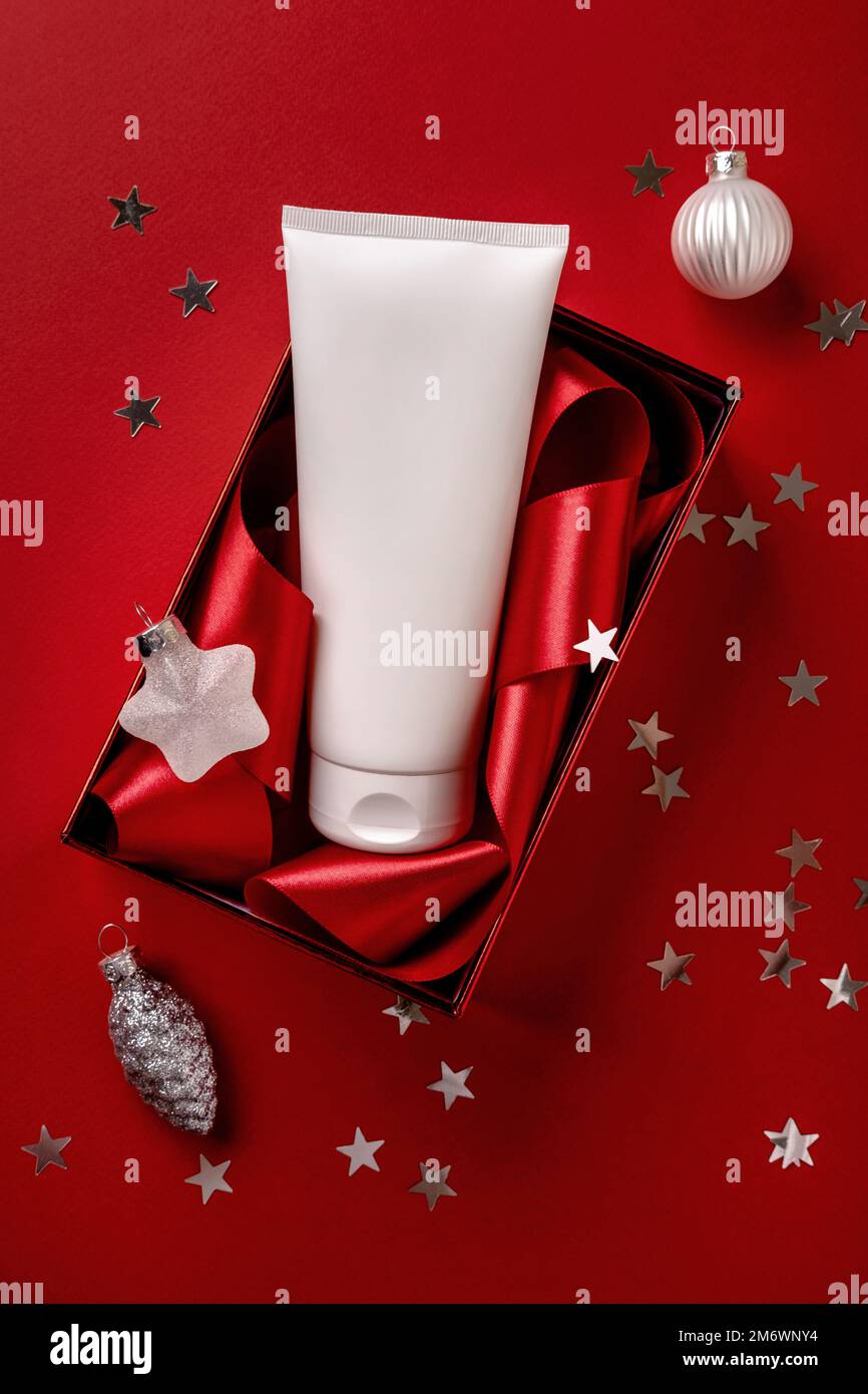 Weißes kosmetisches Produkt in roter geschenkbox auf rotem Hintergrund. Weihnachtsverkauf von Schönheitsprodukten Konzept. Stockfoto