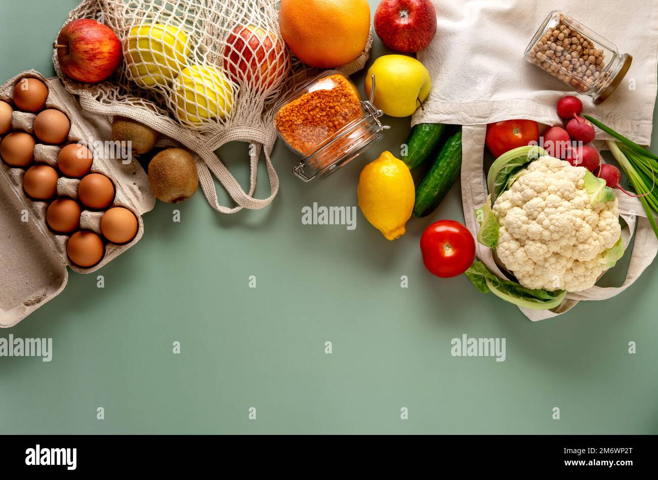 Konzept des „Zero Waste Shopping“ auf grünem Hintergrund. Frisches Gemüse und Obst in umweltfreundlichen Baumwollbeuteln auf dem Tisch. Null-Verschwendung-Konzept Stockfoto