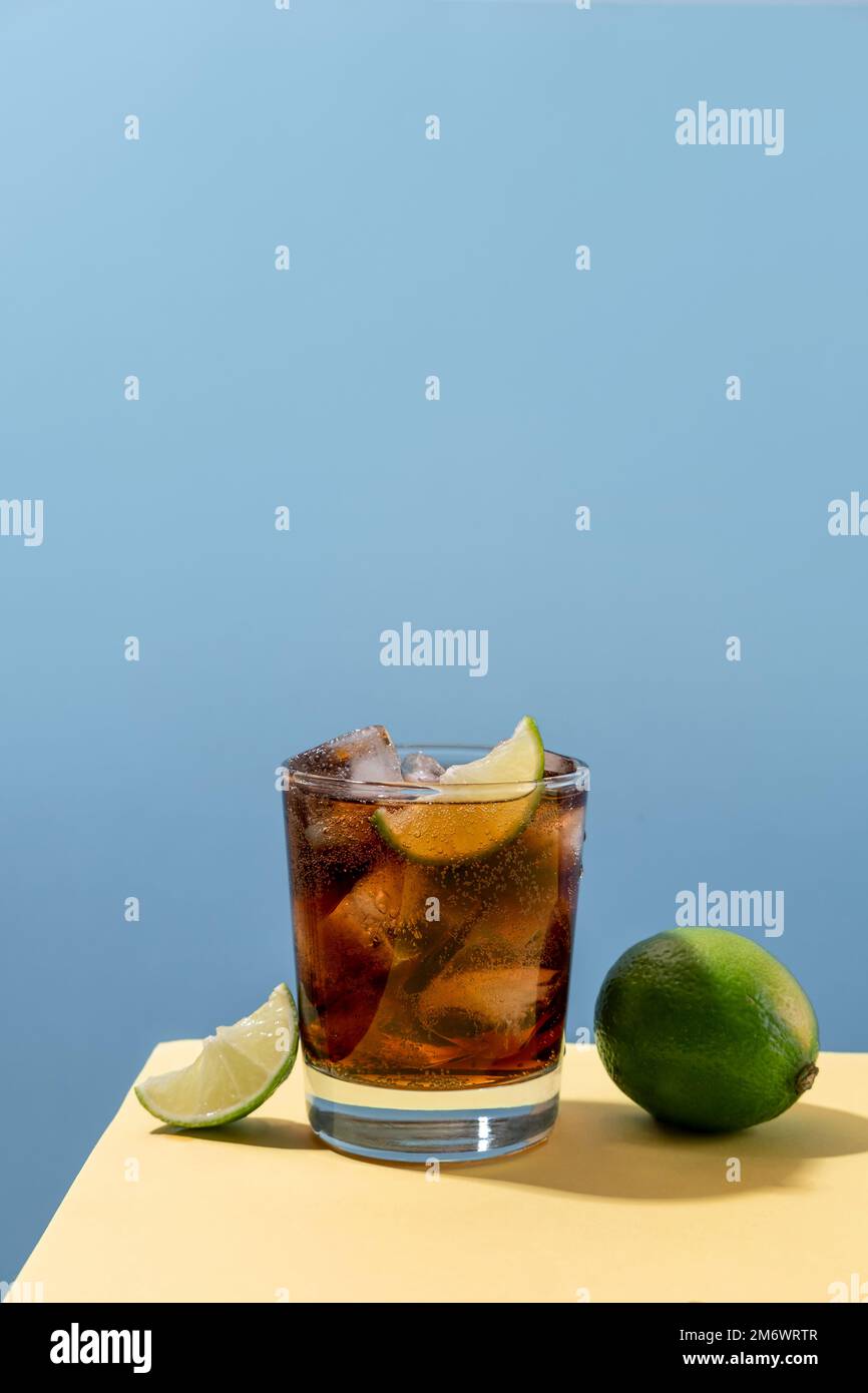 Kuba Libre Alkohol Cocktail mit Limettenscheibe auf blauem Hintergrund. Whiskey-Cola-Cocktail Stockfoto