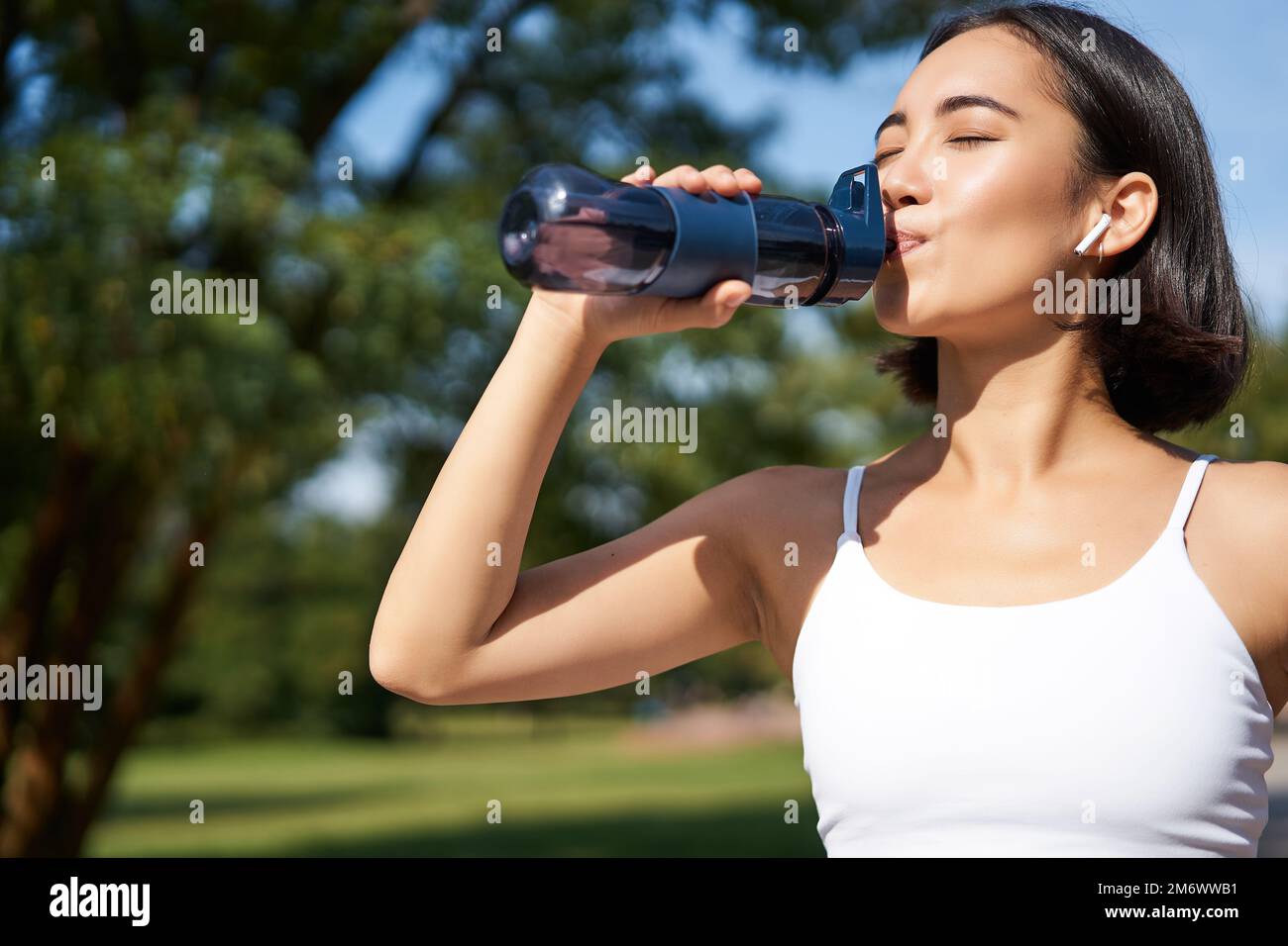 Fit asiatische Sportlerin trinkt beim Marathonlaufen Wasser. Fitness-Girl joggt im Park, trinkt viel. Stockfoto