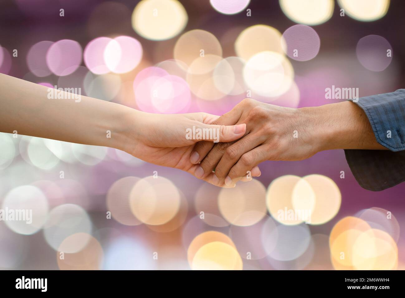 Nahaufnahme Mann und Frau schütteln sich die Hände auf farbigem Bokeh-Hintergrund. Konzept menschlicher Beziehungen. Stockfoto