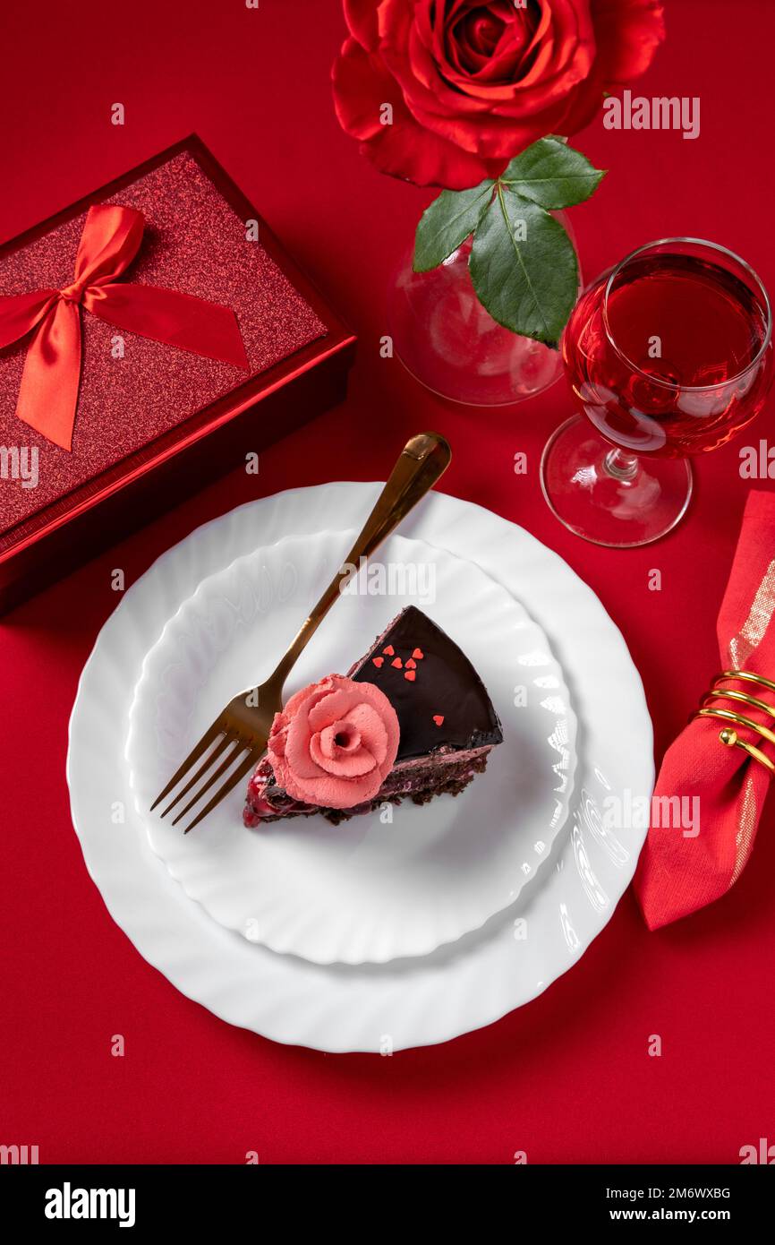 Valentinstag-Abendessen mit Tischdecken mit rotem Geschenk, roten Rosen und Schokoladenkuchen. Blick von oben. Valentinstag di Stockfoto
