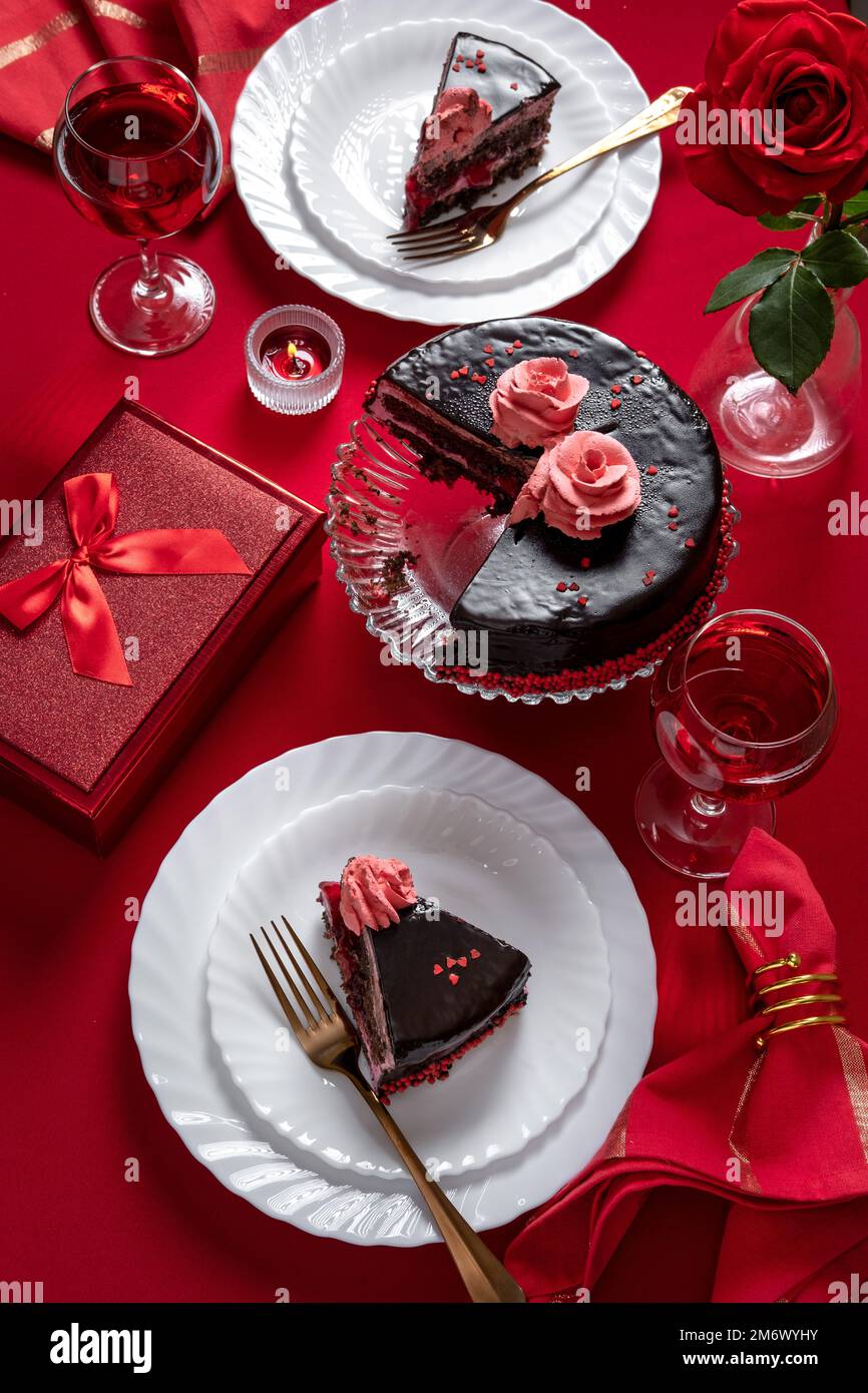 Valentinstag-Abendessen mit Tischdecken mit rotem Geschenk, roten Rosen und Schokoladenkuchen. Blick von oben. Valentinstag di Stockfoto