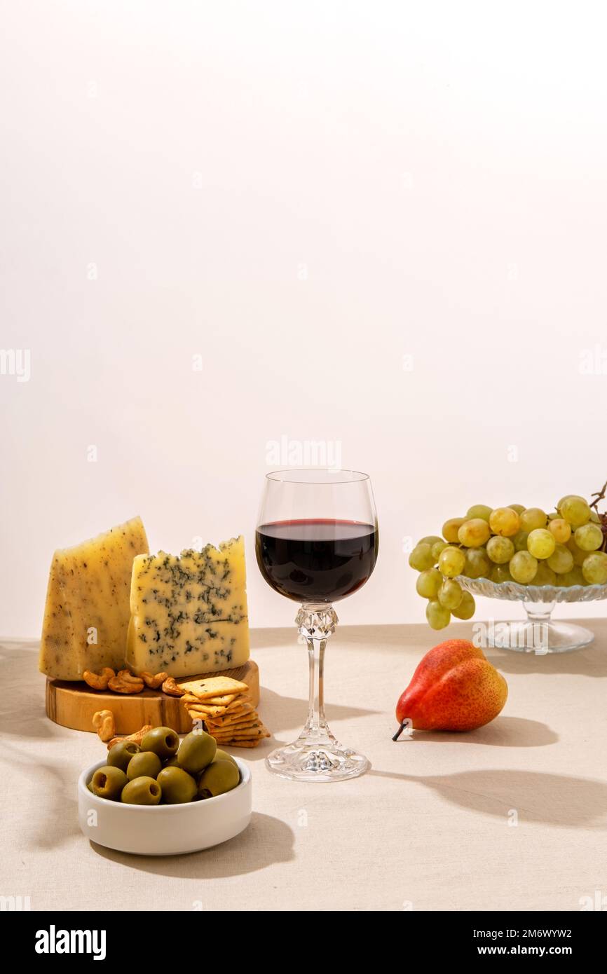 Glas Rotwein mit Trauben, Käse und Salami auf hellem Tischhintergrund. Rotwein mit Käse und Obst. Platz für Text Stockfoto