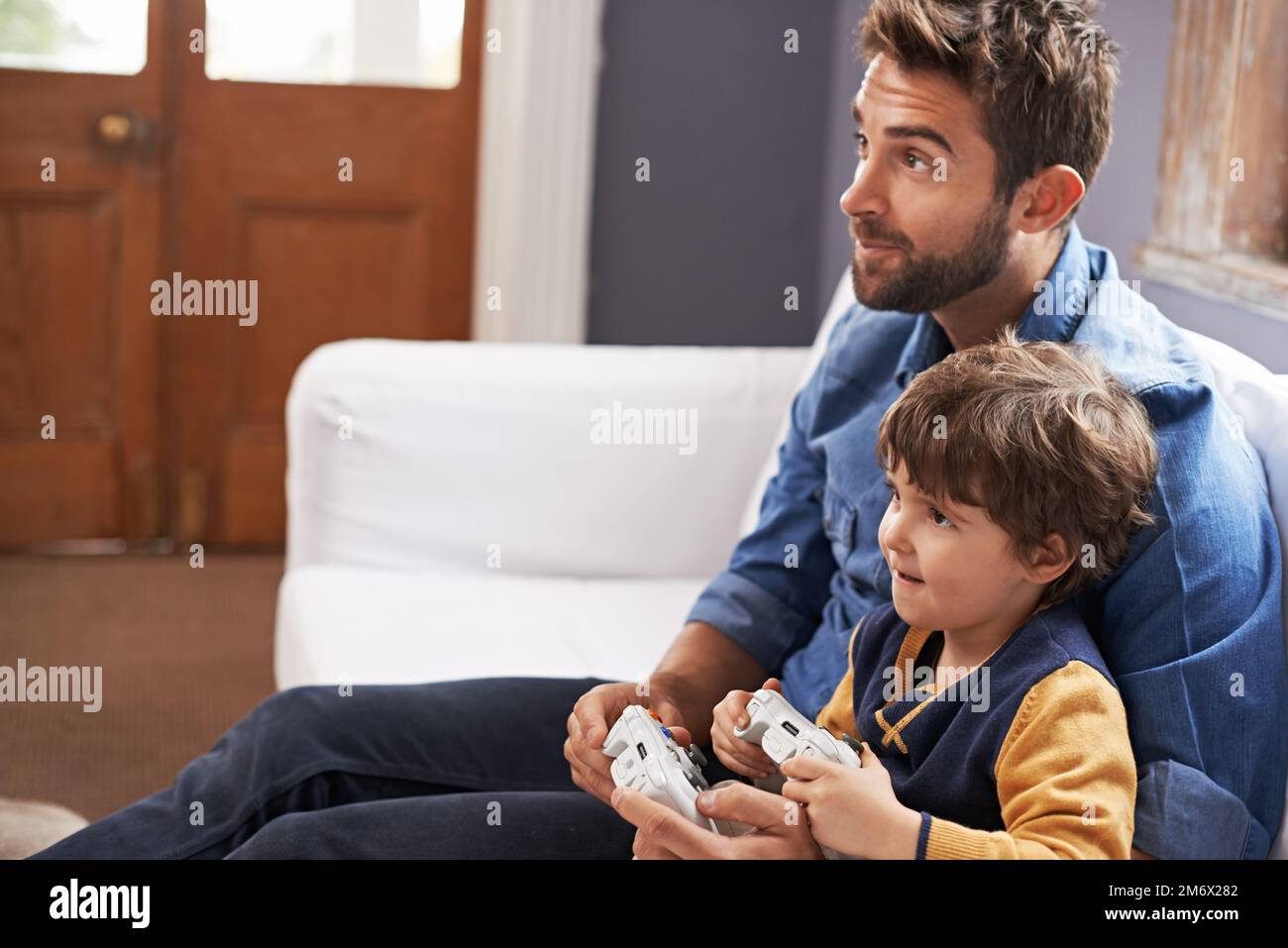 Er hat die Kontrolle über diese Runde. Ein gutaussehender Vater und sein süßer Sohn spielen zusammen ein Videospiel. Stockfoto