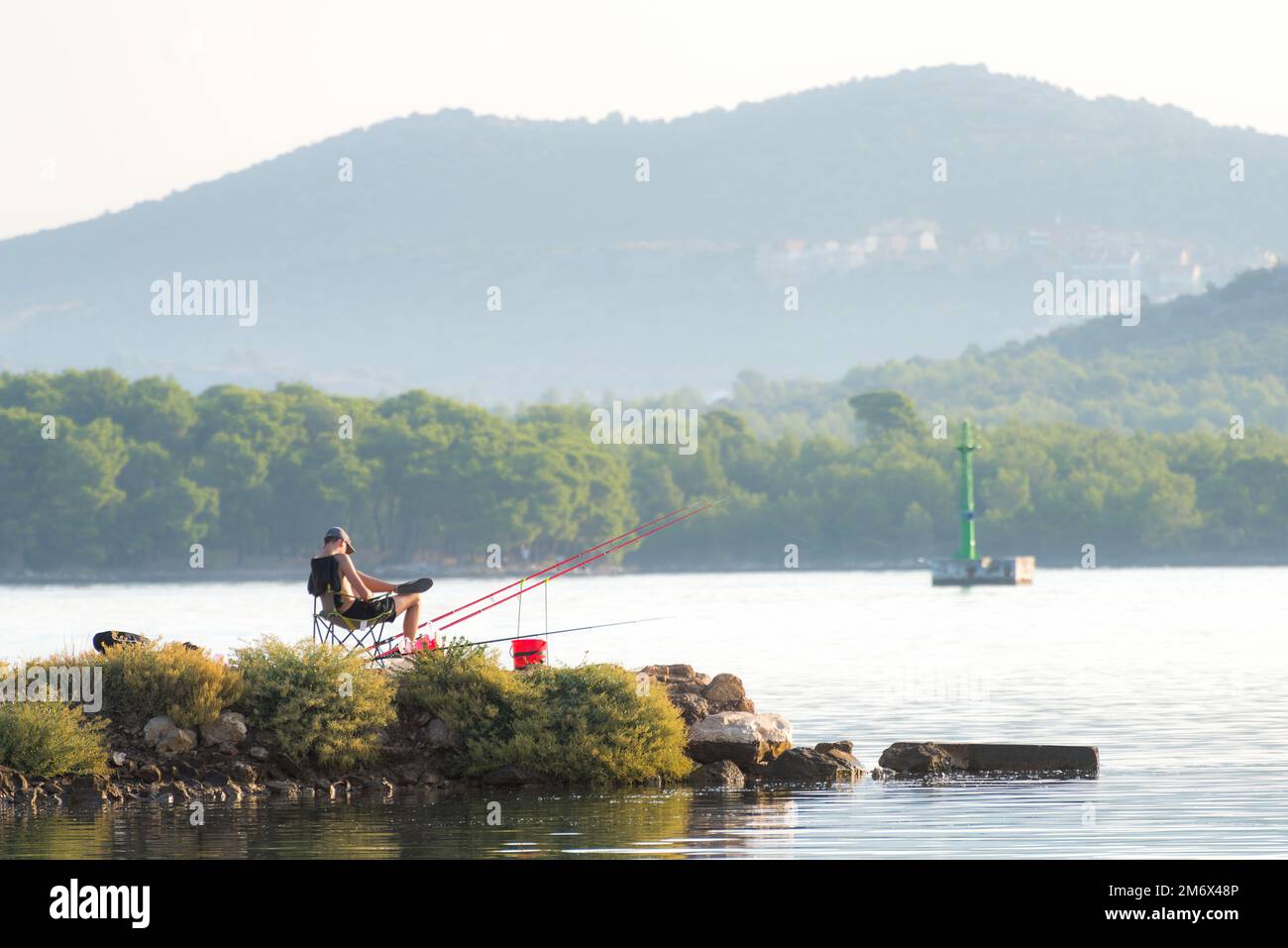 Der junge Mann sitzt und angelt auf dem Kanal sveti ante in sibenik kroatien Stockfoto