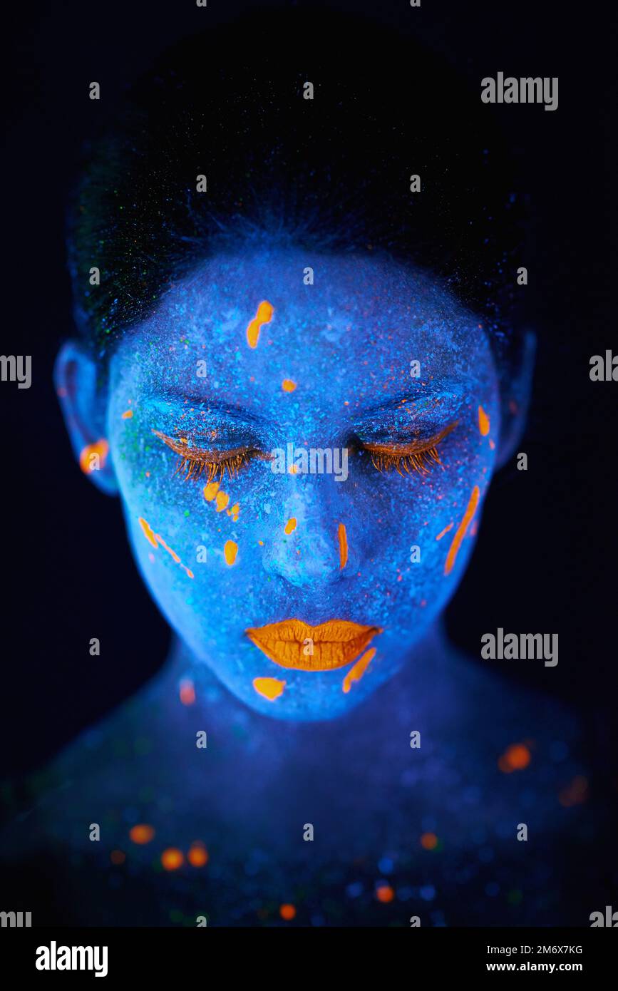 Neongöttin. Eine junge Frau, die mit Neonfarbe im Gesicht posiert. Stockfoto